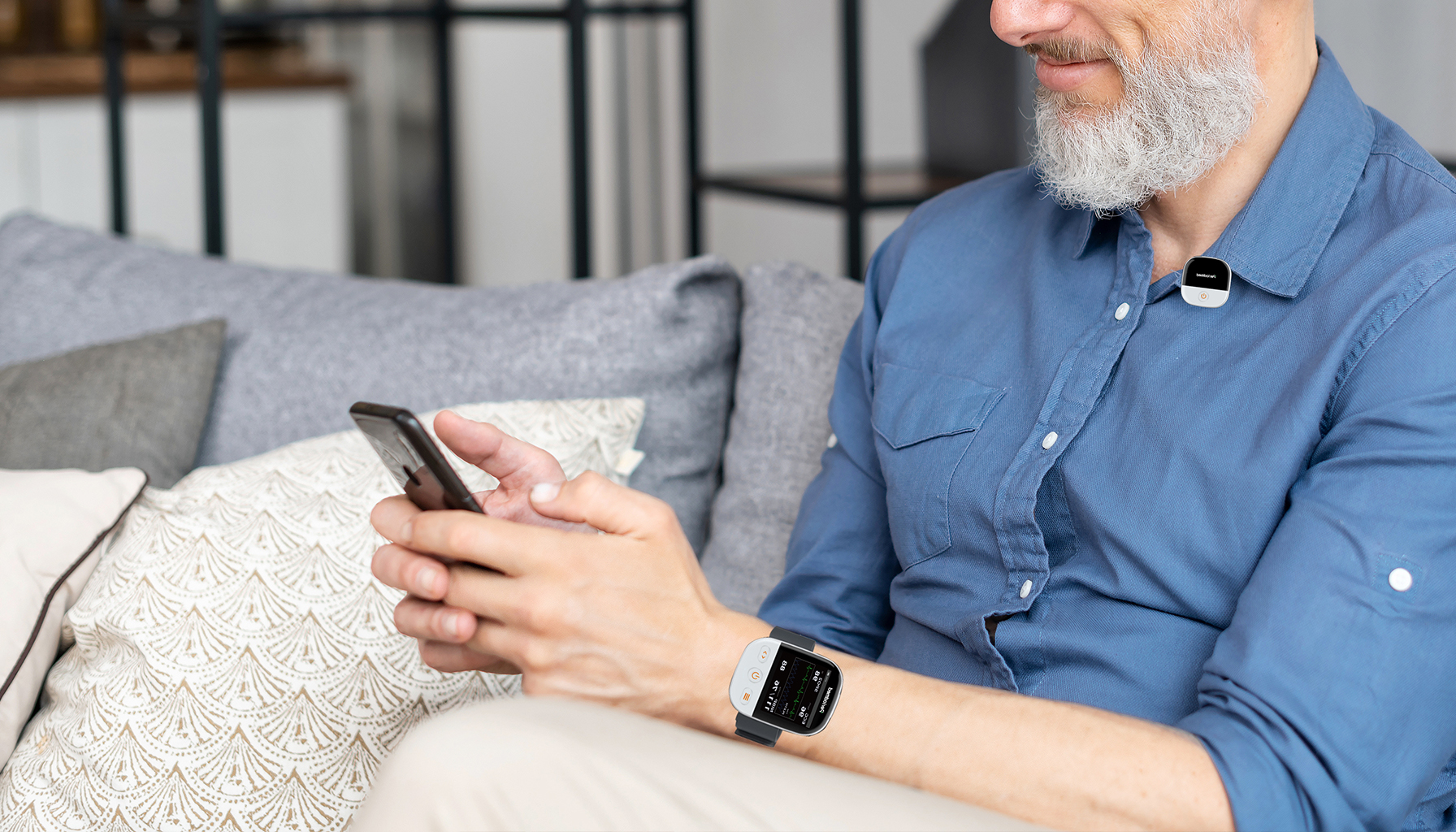 Elder wearing upper-arm wearable telemetry monitor at home, family checking health data on phone together